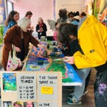 members of the public take part in a Figment Arts workshop, they are standing around a long table painting the Sussex Knucker painting
