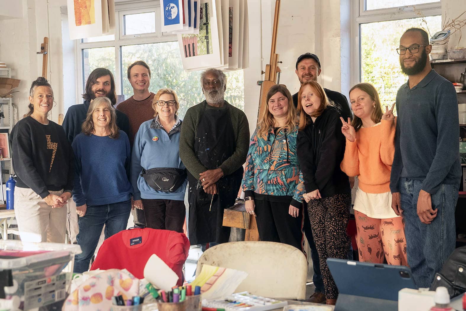 A group of people are standing in an art studio, they are smiling and looking at the camera