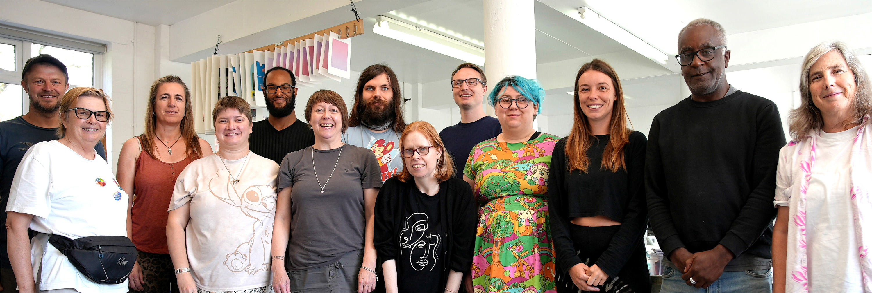 a group of people are standing and smiling at the viewer, they are in a bright, sunny art studio
