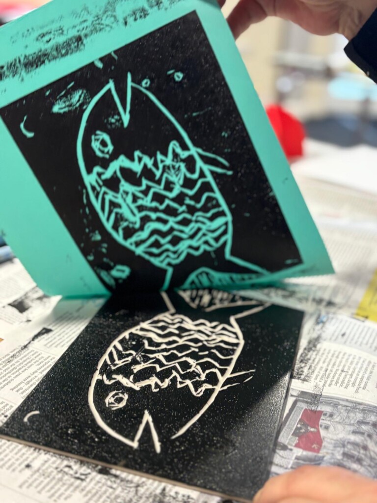 a Lino cut print of a fish on turquoise coloured paper