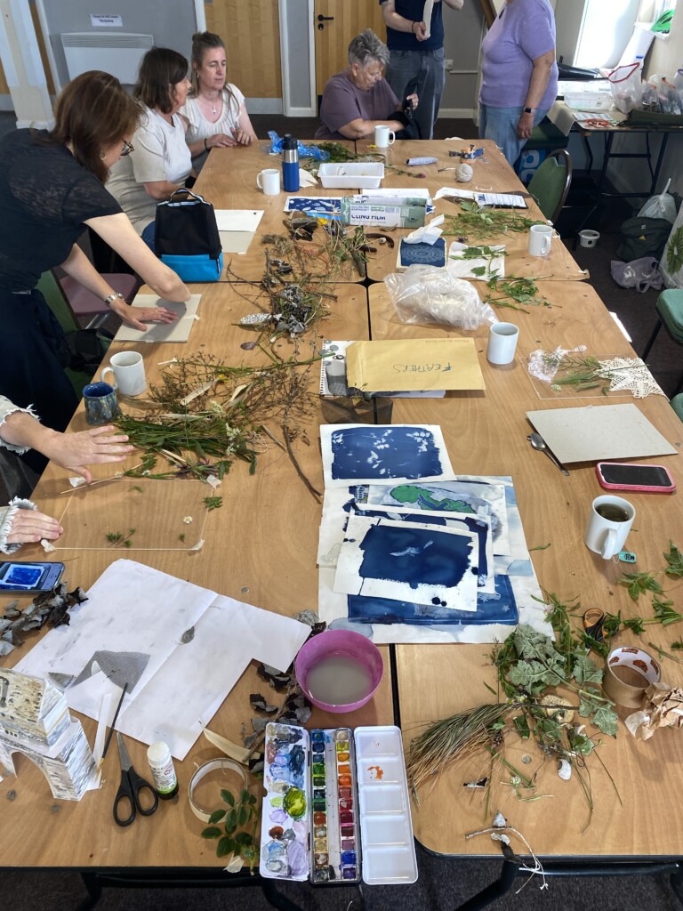 a group of people around a table making Cyanotype prints, using leaves and foliage to create patterns on the paper