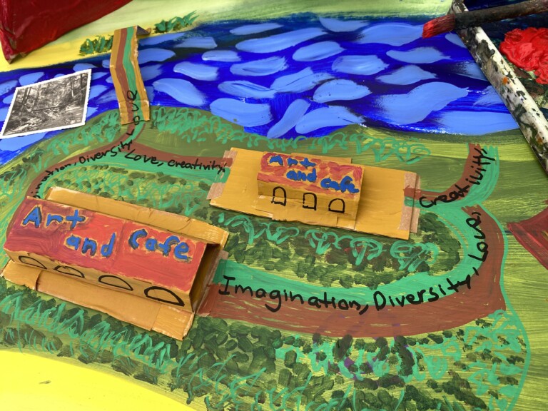 a bright painted map of a green grassy area next to some water. There are buildings and on the roof it says 'art and cafe'