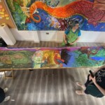 an overhead photo, looking down onto a long painting which depicts the Devil's Dyke legend. people are stood around the painting.
