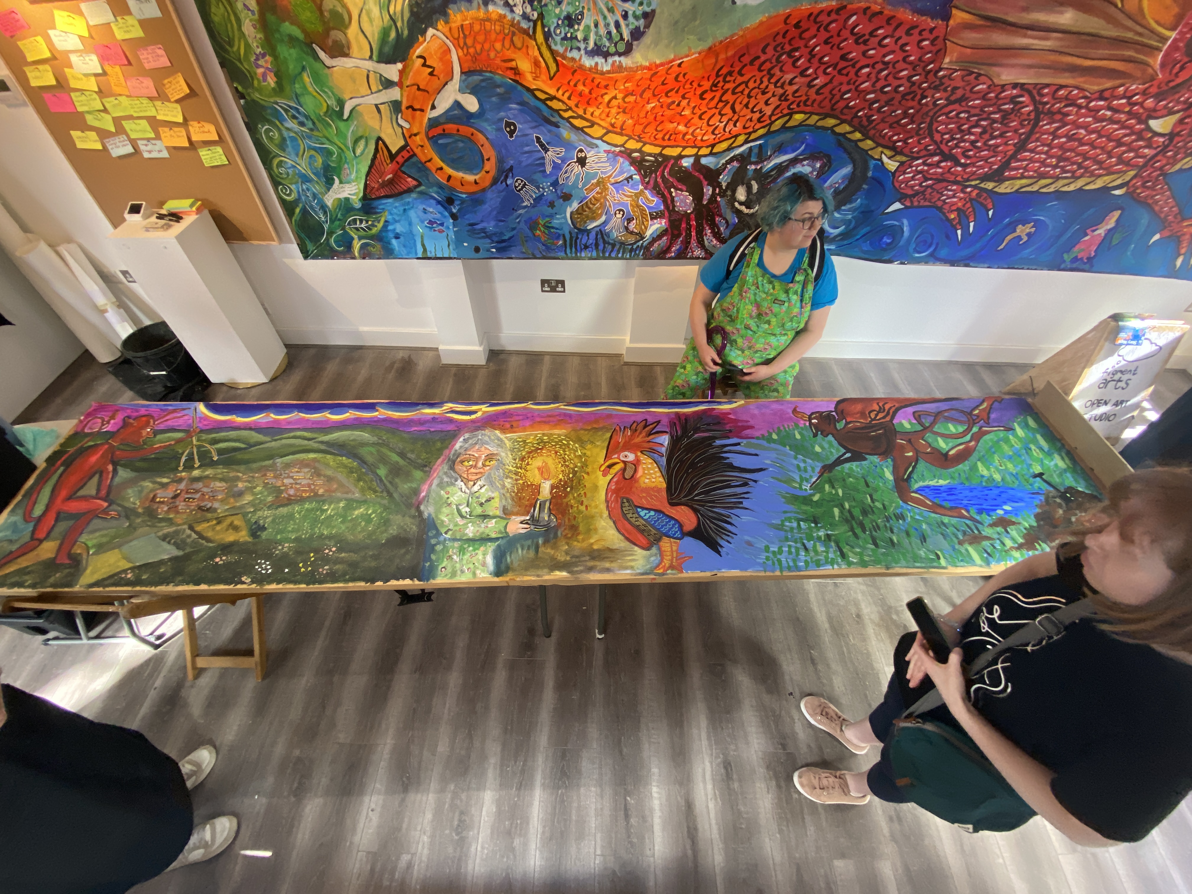 an overhead photo, looking down onto a long painting which depicts the Devil's Dyke legend. people are stood around the painting.