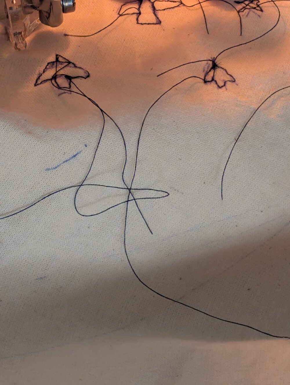 a close up of some embroidery, black thread on a white canvas. The embroidery is in the shape of small birds