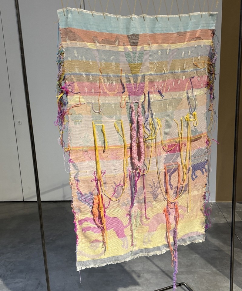 a colourful fabric hanging, oranges, reds, yellows and blues, with threads and stitches worked into it