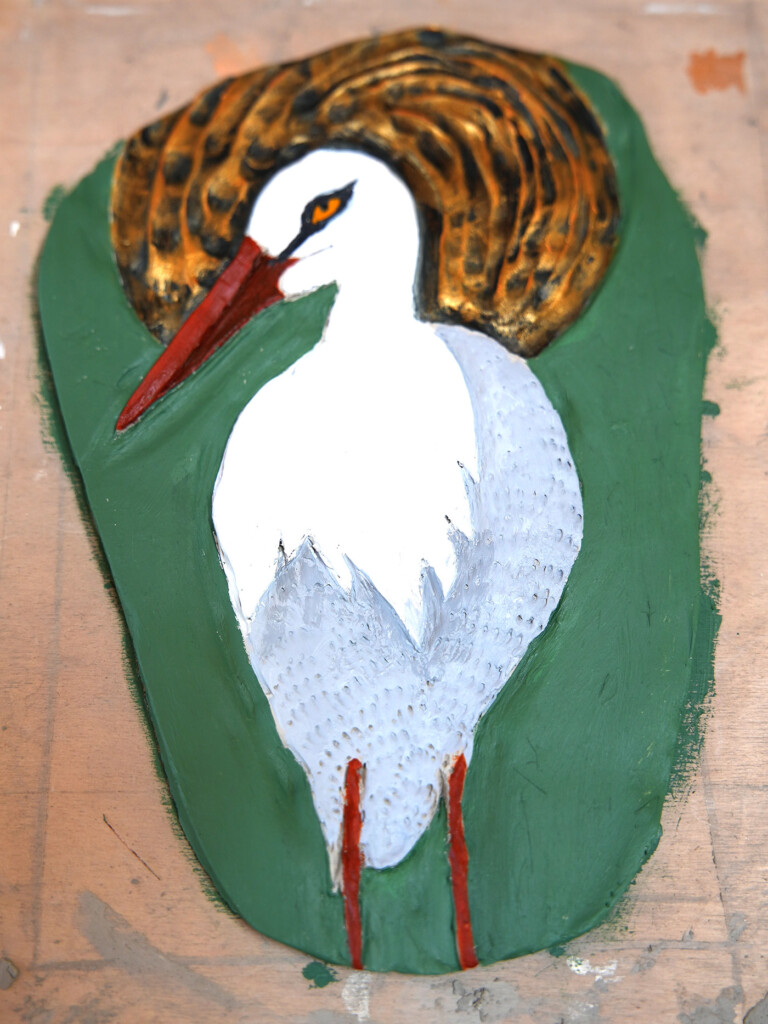 a painted, relief image of a stork, the background is green and gold