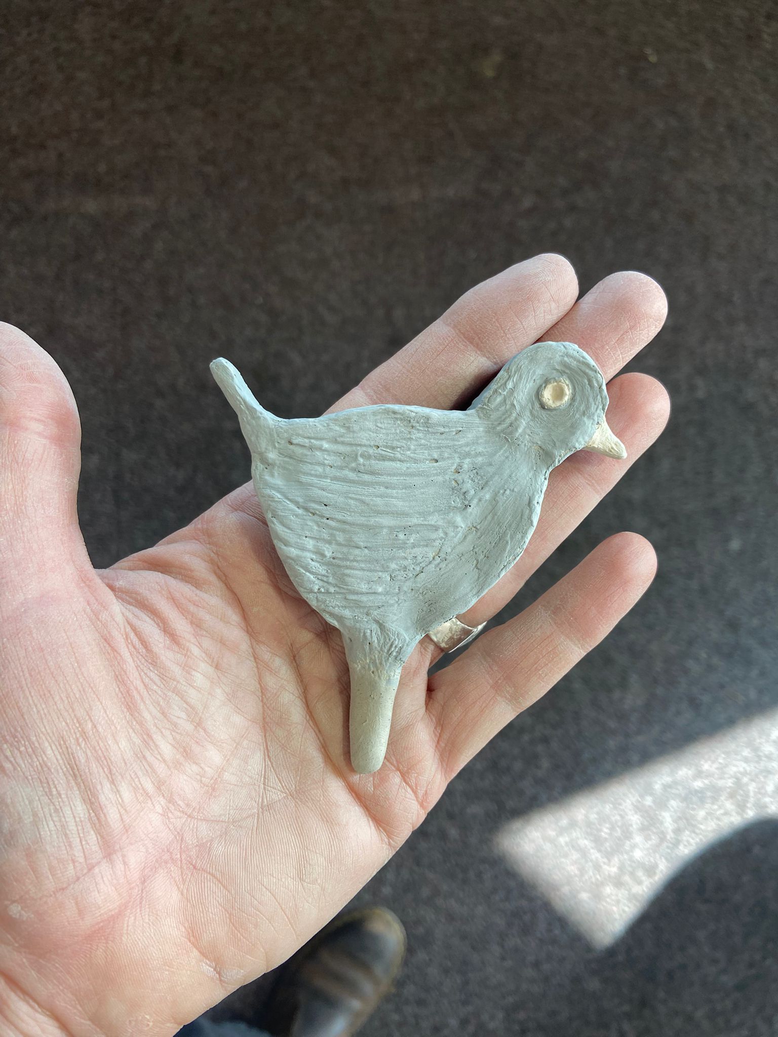 a hand holds a clay bird, it is painted green with a yellow beak and eye