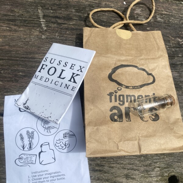 a brown paper bag, containing a small glass bottle and a written pamphlet which says 'make your own charm'