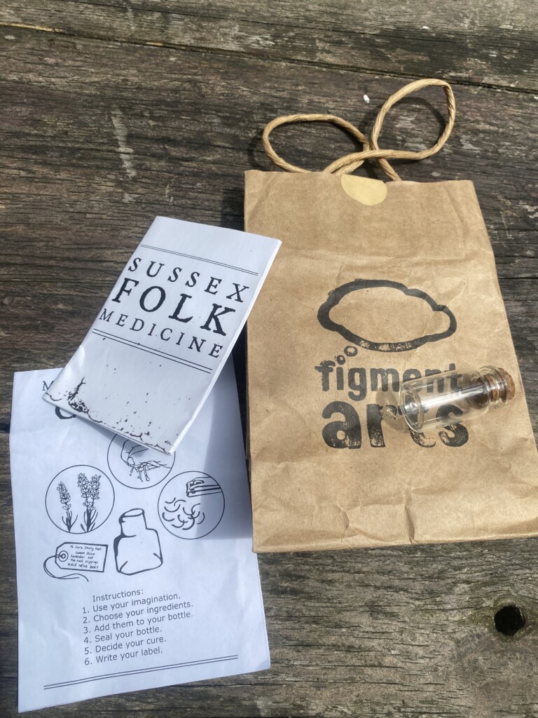 a brown paper bag, containing a small glass bottle and a written pamphlet which says 'make your own charm'