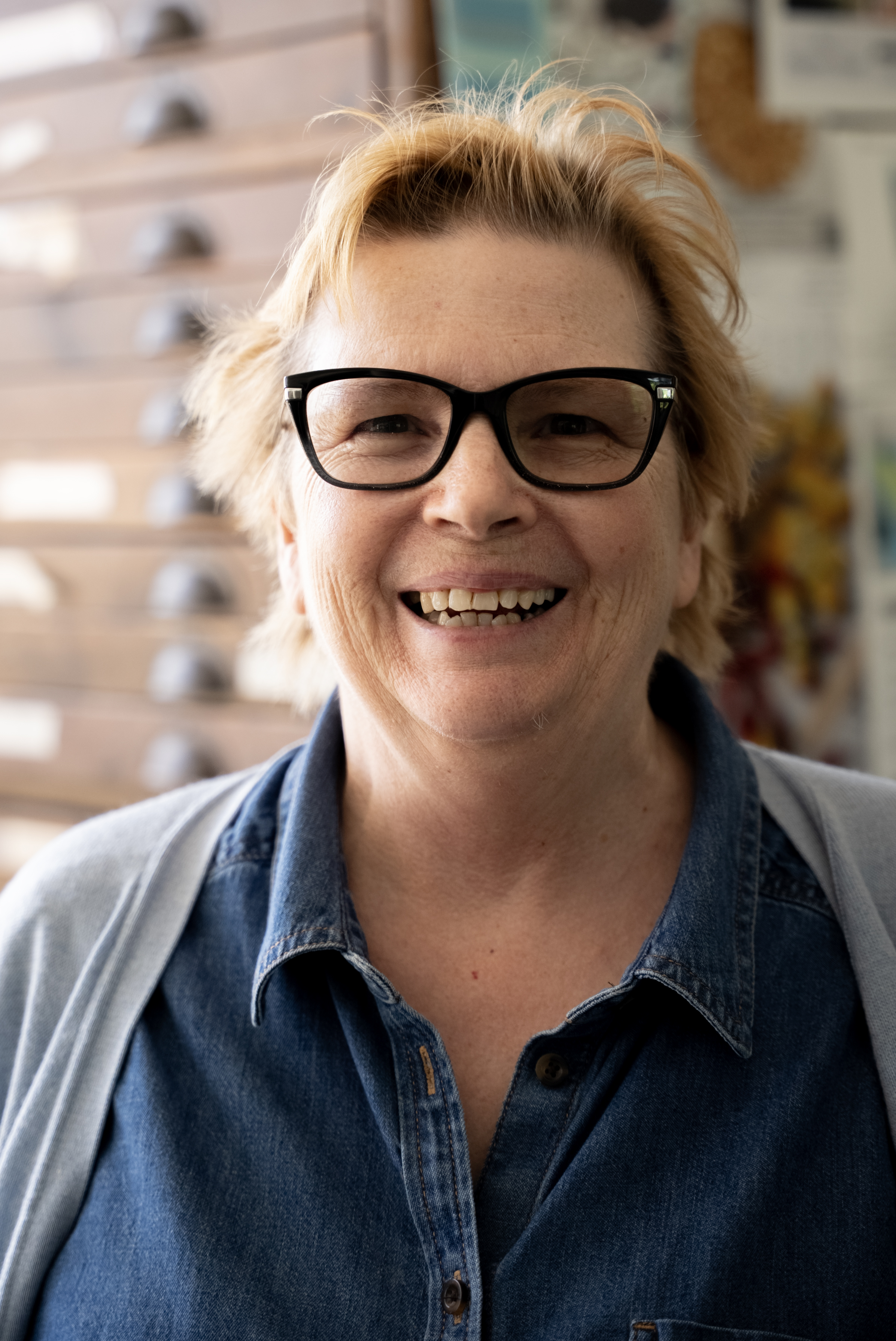 Debbie is a woman with short reddish hair and dark rimmed glasses, she is looking at the camera and smiling